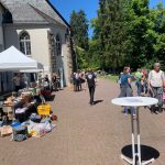 Waldhof-Gelände mit Flohmarktständen und Besucher:innen des Flohmarktes bei sonnigem Wetter.